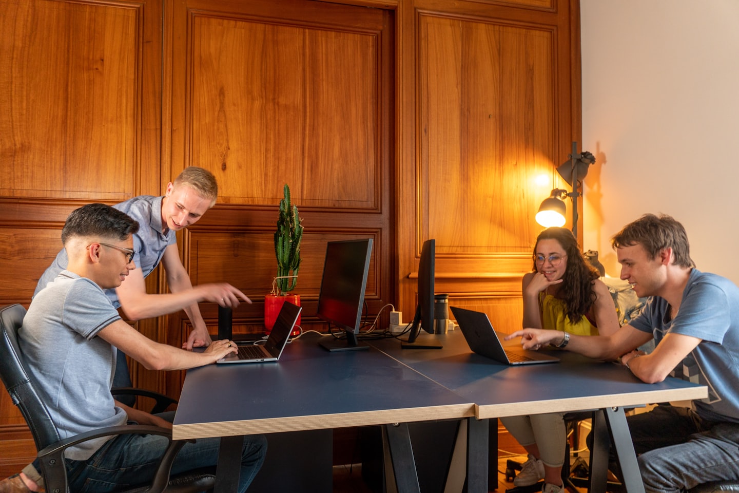 Cztery osoby współpracujące przy biurku z laptopami.